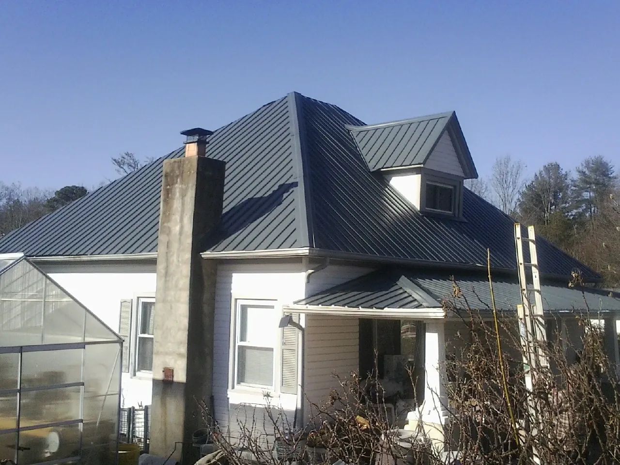 Dark blue standing seam metal roof on a white farmhouse with dormer — Slate & Tile Roof Repair by Roofing Brothers in Lyman