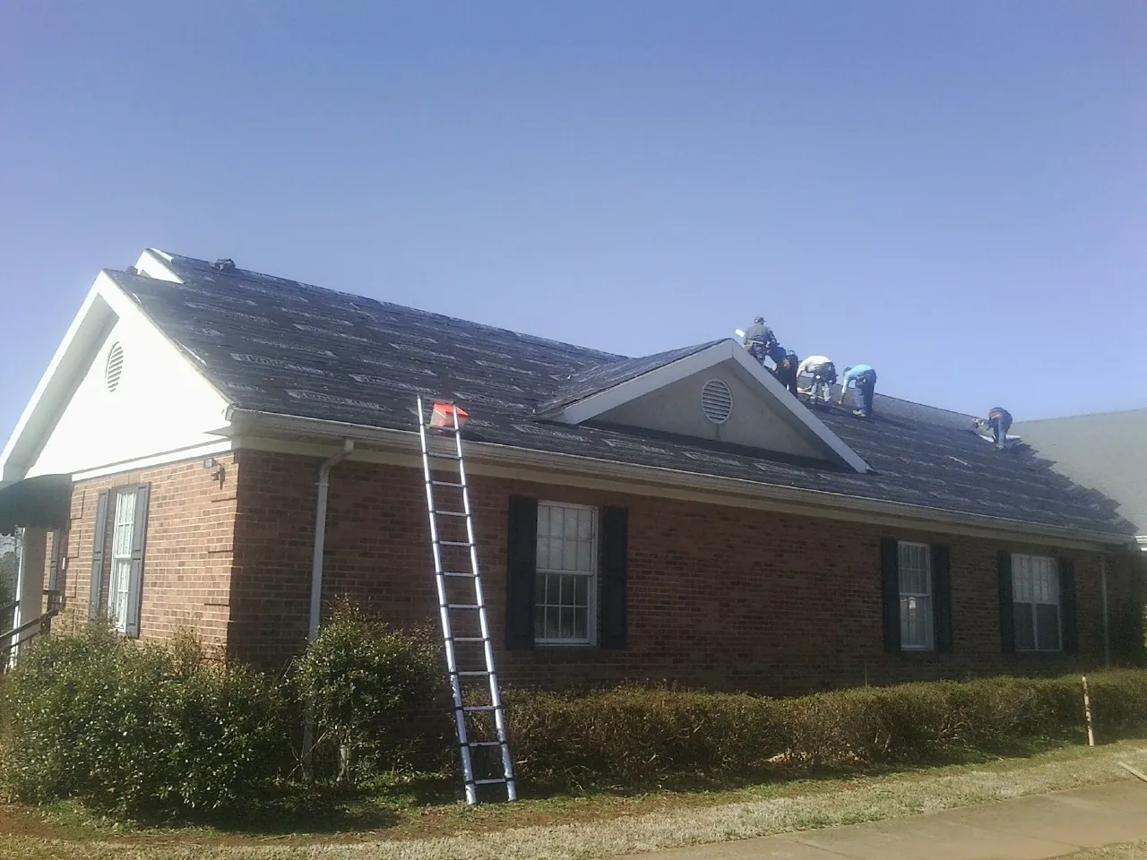 Crew tearing shingles off a brick ranch roof with a ladder set — Emergency Roof Repair work by our crew in Lyman