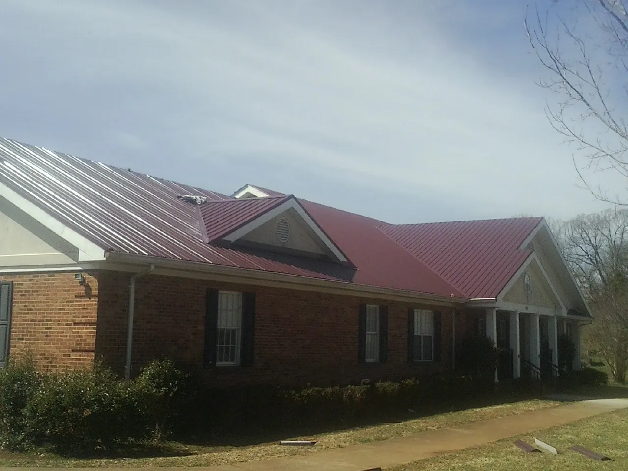 Red metal roof with gabled entries on a long brick building, from a Hail Damage Roof Repair job in Lyman