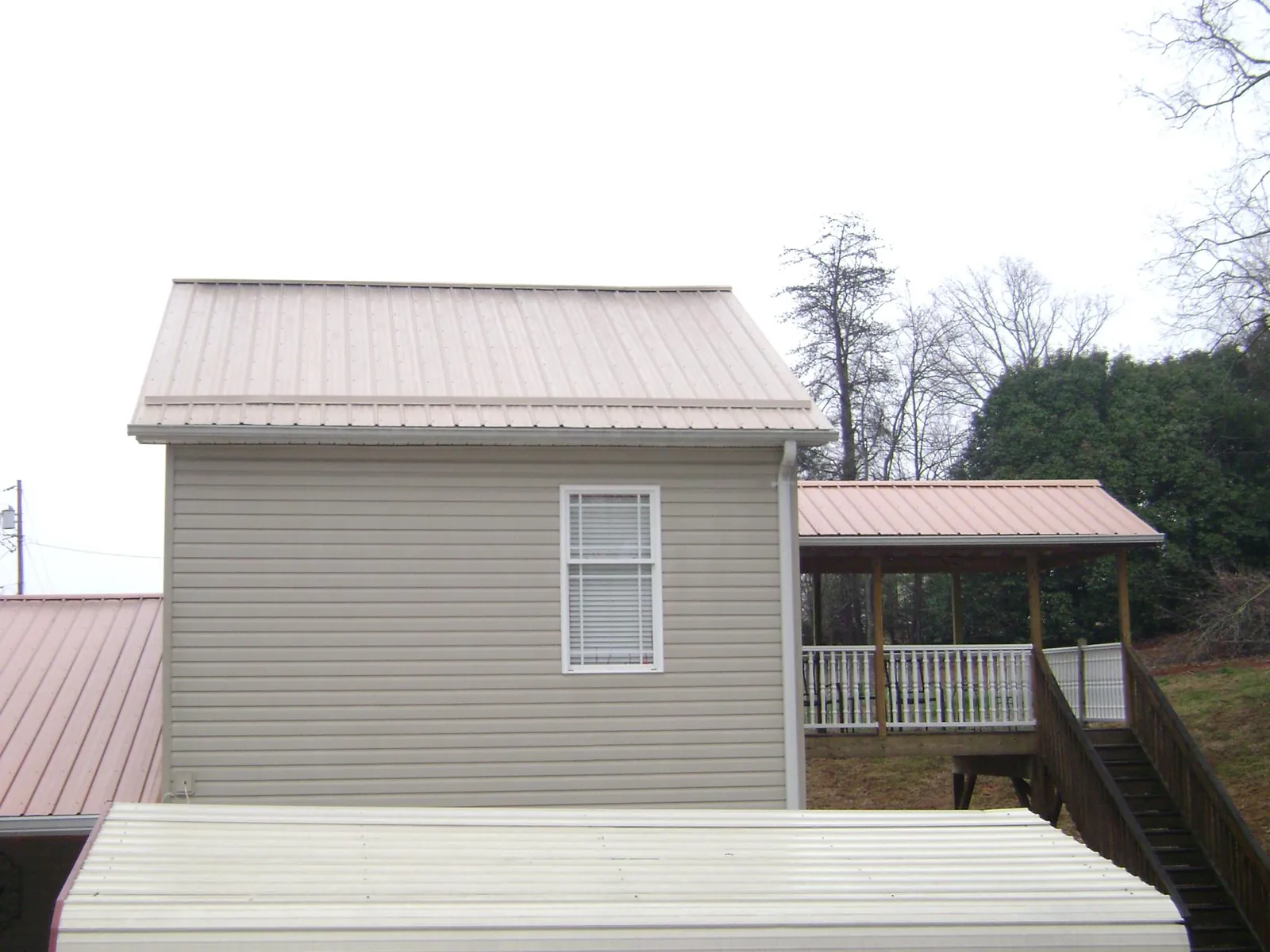 Tan metal roofs on a two story addition and attached porch, from a Roof Replacement job in Lyman